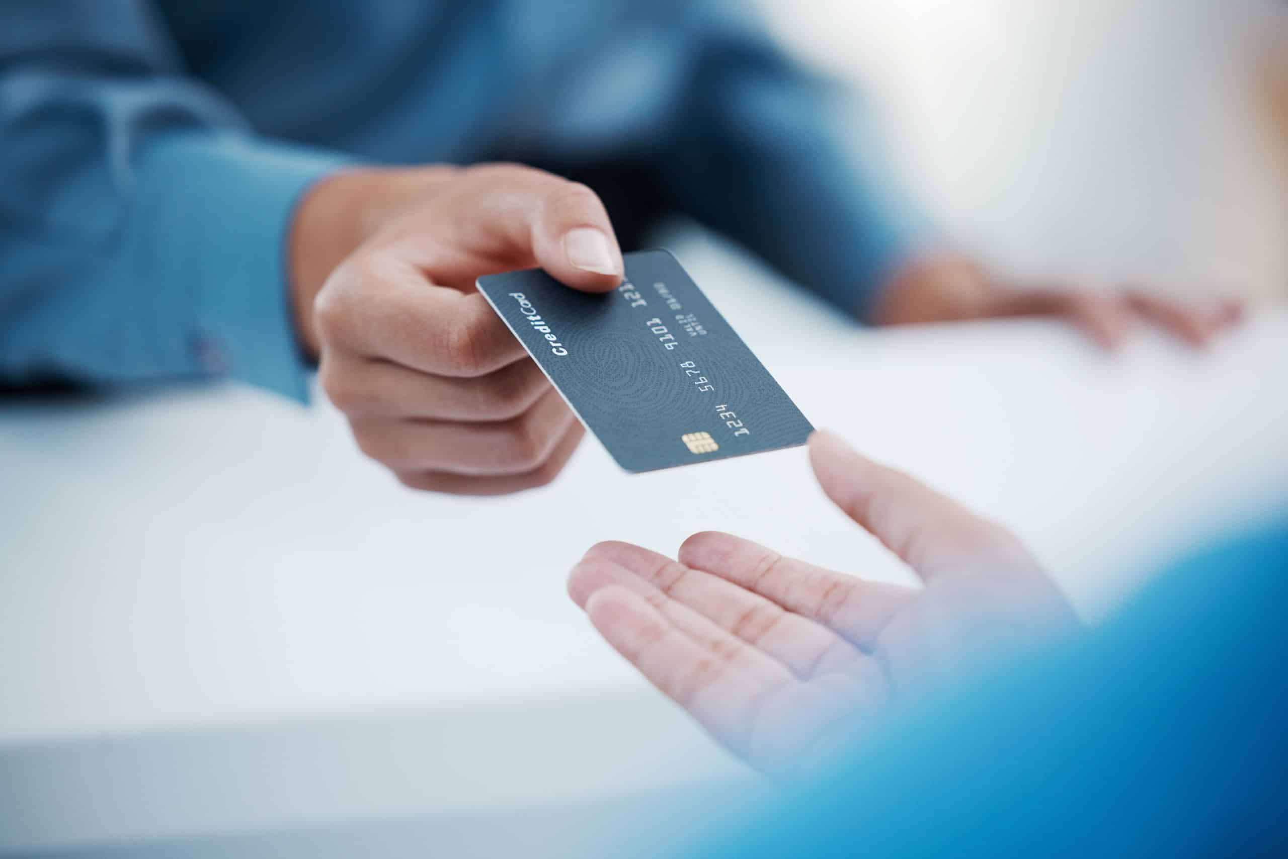 Person handing a blue credit card to another person for payment.